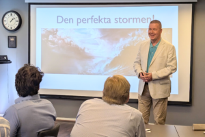 En man i vit kavaj står framför en storbildskärm